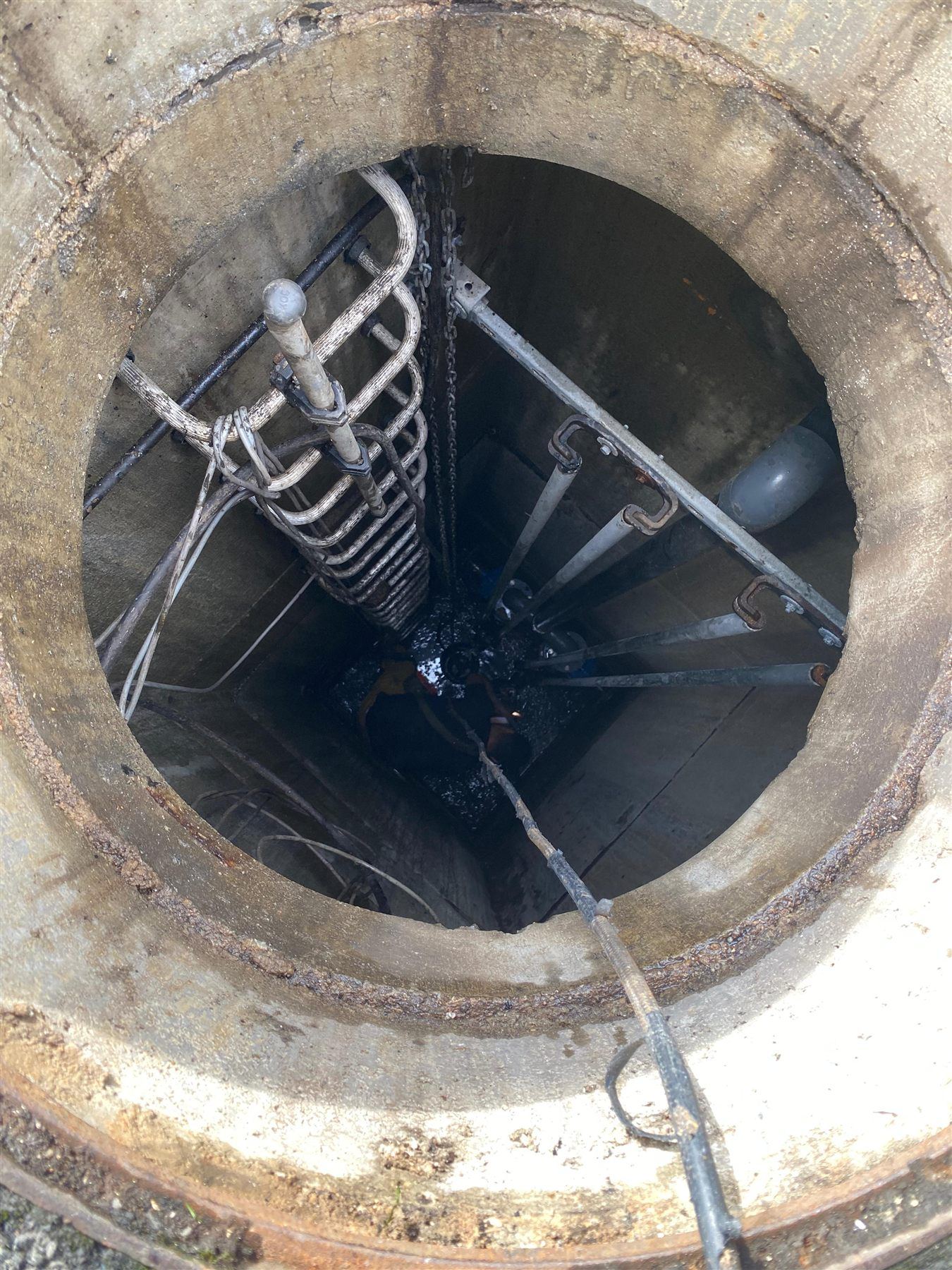 Vue plongeante dans un poste de relevage profond en béton pendant l'intervention